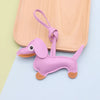 A small, purple dachshund leather keychain charm is displayed on a light wooden surface.