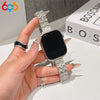 A hand is holding a black Apple Watch with a sparkling metal fishscale band and a gold ring.
