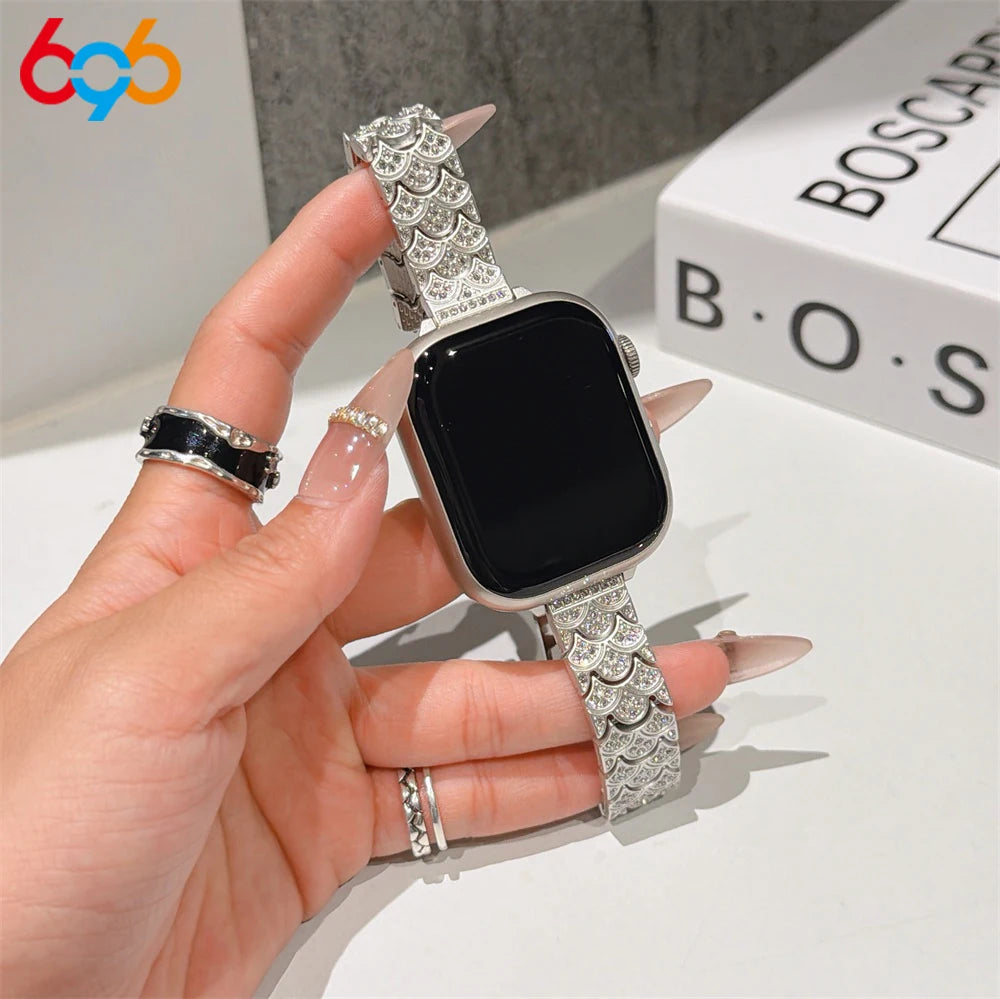 A hand is holding a black Apple Watch with a sparkling metal fishscale band and a gold ring.