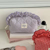 Red and white checkered makeup pouch with lace trim resting on a white surface next to a book.