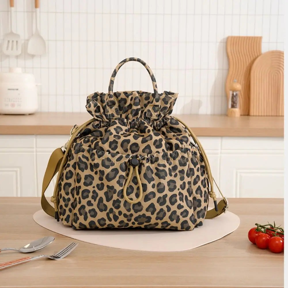 A brown leopard print insulated lunch bag with a drawstring closure resting on a wooden table.