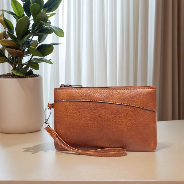 A brown retro PU leather zipper wrist bag resting on a light surface next to a potted plant.