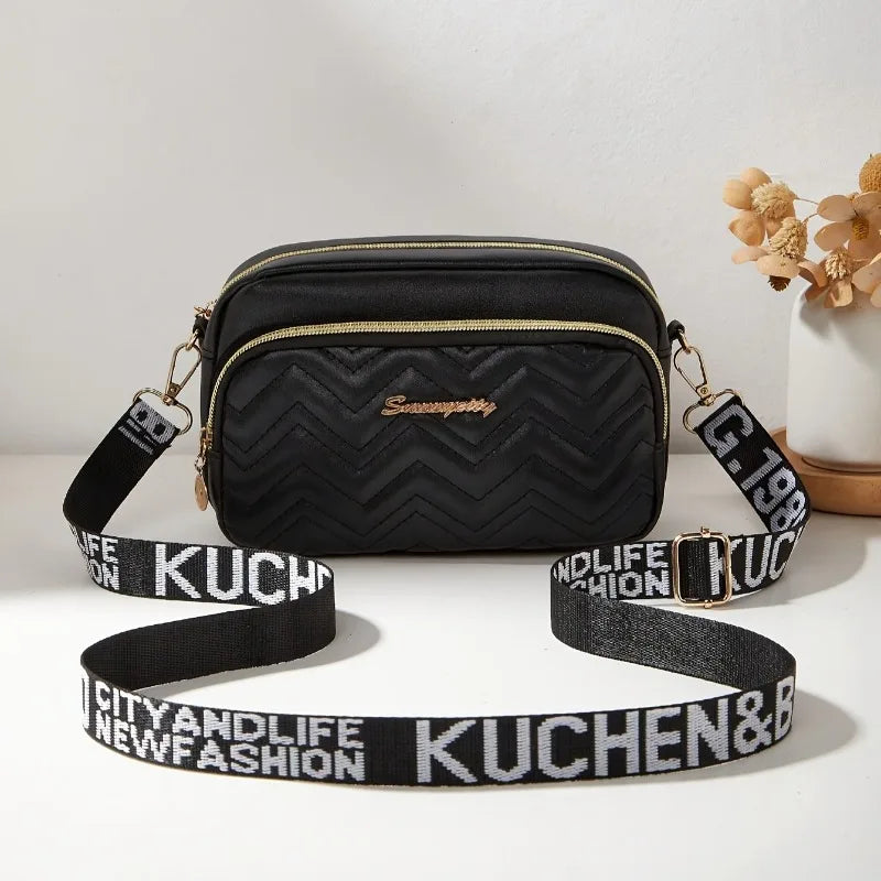 Black quilted crossbody camera bag with a gold chain strap and matching fabric strap.