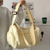 A beige canvas crossbody travel tote bag is being held by a person against a white background.