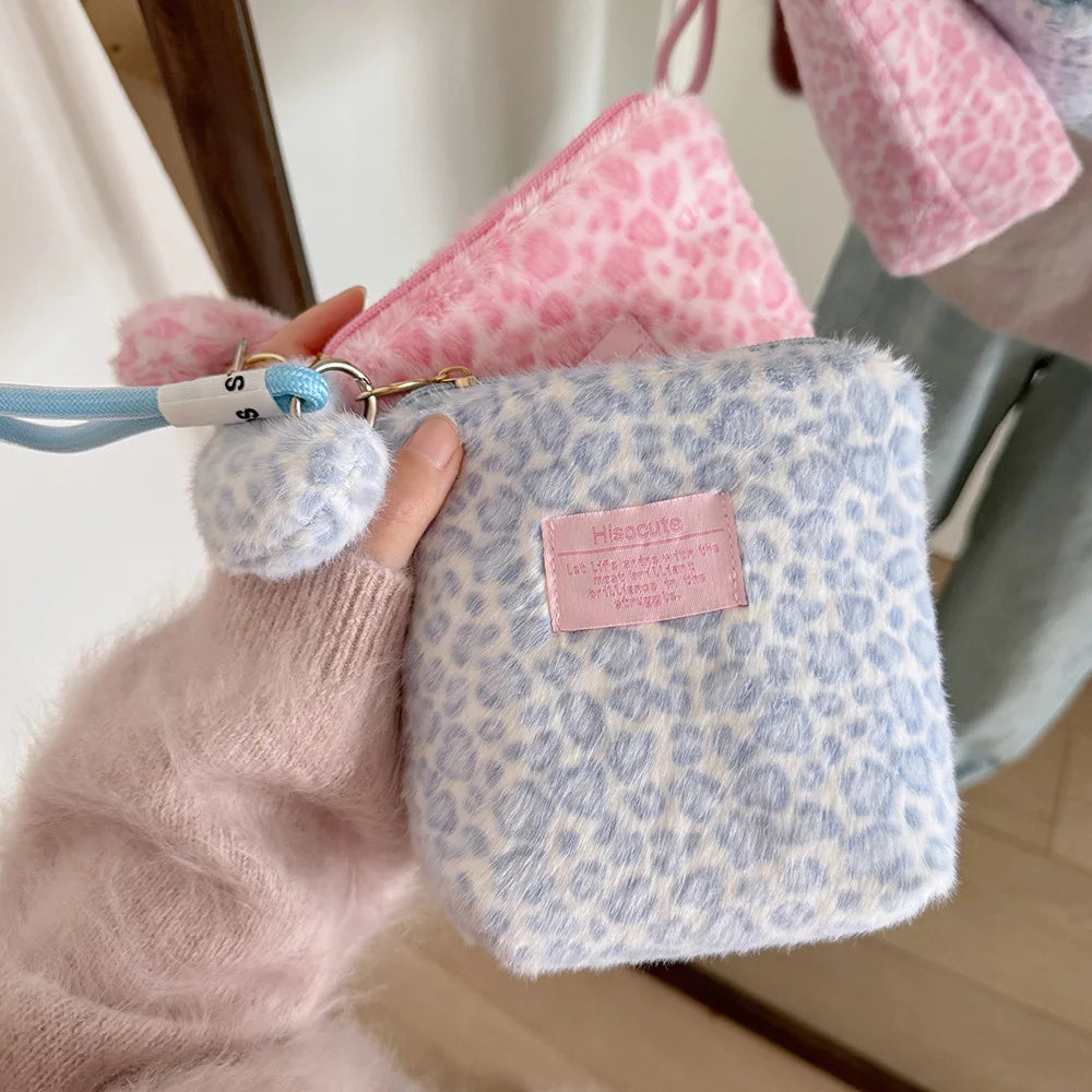 A hand holds a light blue leopard print makeup bag with pink and white fuzzy lining.
