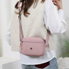 A woman is wearing a light beige nylon crossbody bag with a pink accent and a wide strap over a white shirt.