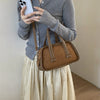 A woman holds a brown leather mini crossbody bag while taking a photo with her smartphone.