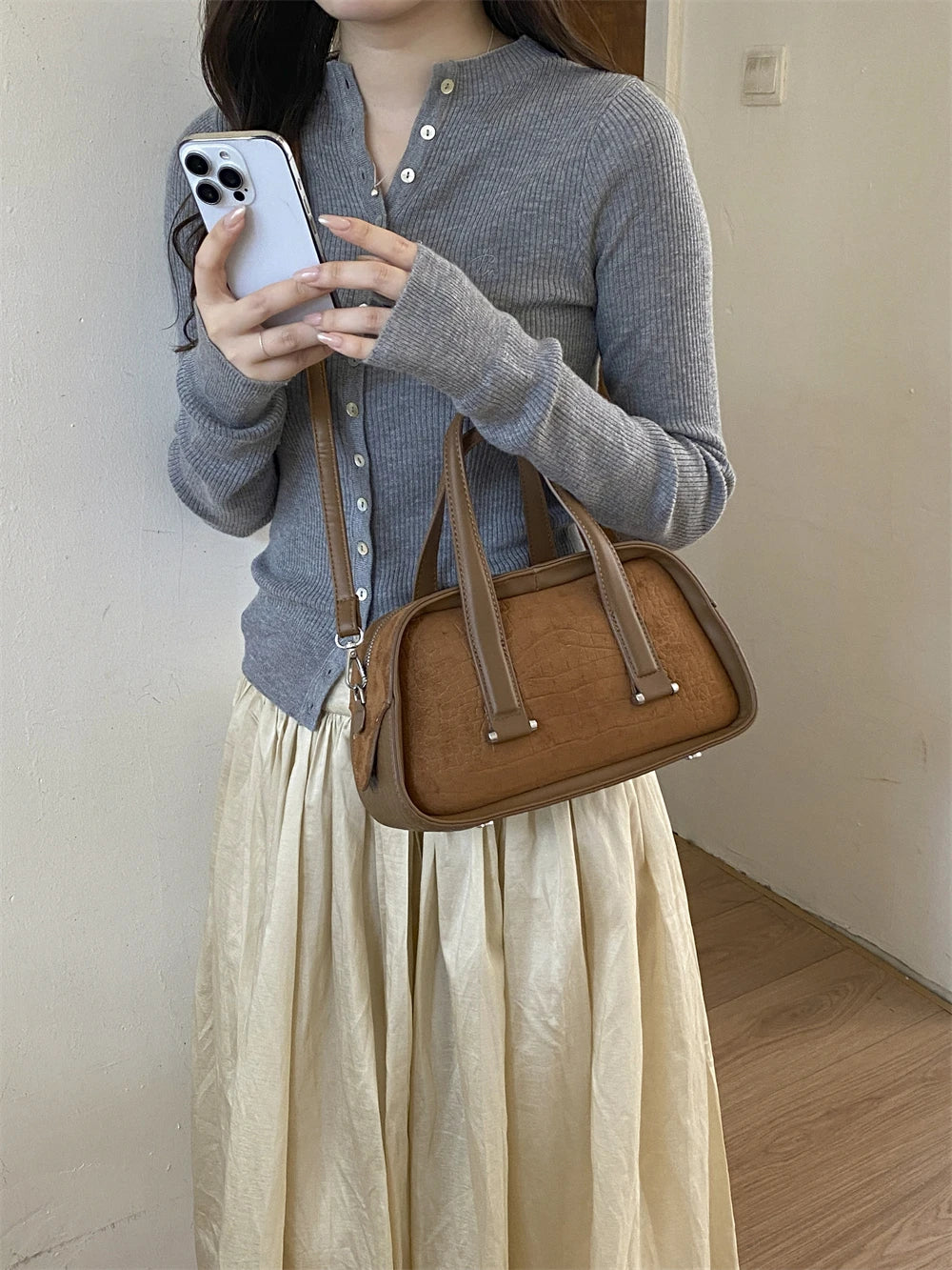 A woman holds a brown leather mini crossbody bag while taking a photo with her smartphone.