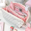 A pink and white polka dot shell pencil case is shown open, revealing various pens and cosmetic items.