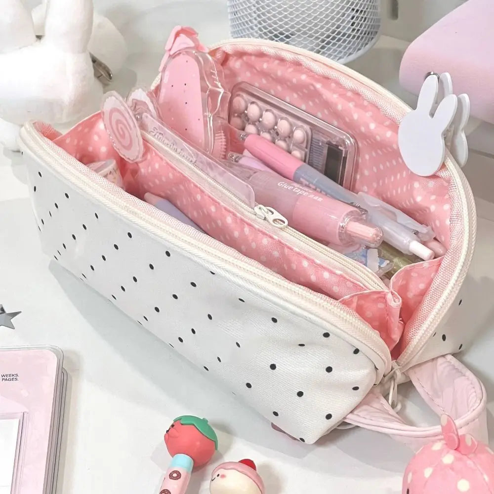 A pink and white polka dot shell pencil case is shown open, revealing various pens and cosmetic items.