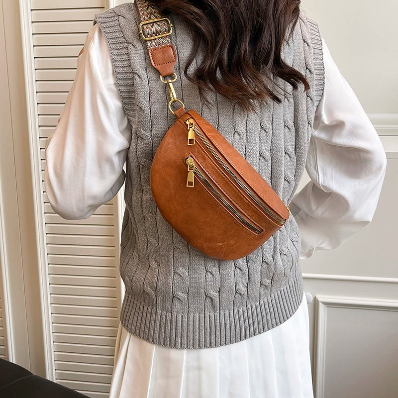 A woman wears a gray knitted vest over a white shirt, featuring a brown leather crossbody bag with a gold-toned strap.