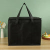 Black reusable insulated cooler bag with handles sitting on a wooden surface.