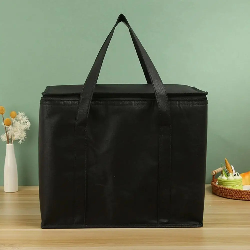 Black reusable insulated cooler bag with handles sitting on a wooden surface.