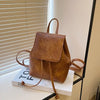 Mini sac à dos en cuir marron à cordon, exposé sur une boîte blanche près d'un store.