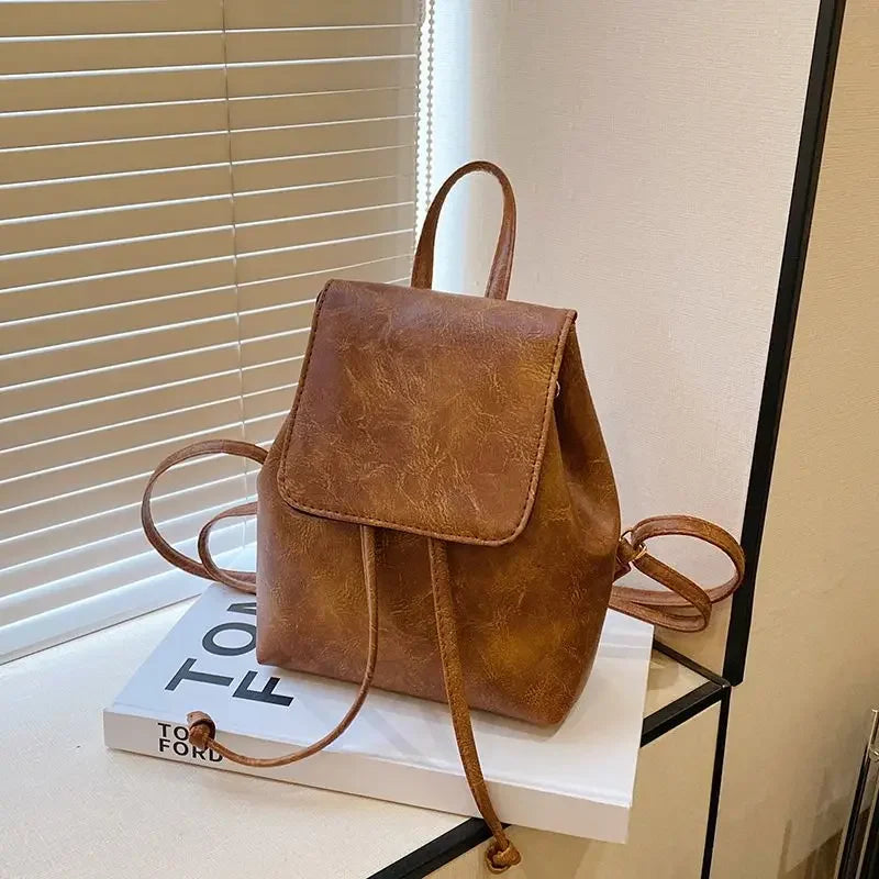 Mini sac à dos en cuir marron à cordon, exposé sur une boîte blanche près d'un store.