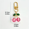 Gold-toned keychain featuring green leaves and pink fruit charms.