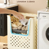 A person is placing folded laundry into a light-colored, square mesh basket with handles, next to a white washing machine.