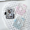 A white quilted surface holds three clear acrylic photo card holders with pink, purple, and blue accents.