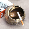 Vintage metal ashtray with a rose embossing and windproof lid resting on a light gray surface.