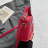 A vibrant red leather crossbody bag with silver hardware is shown next to a gray blazer and a book.