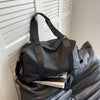 A black Versatile Oxford Cloth Travel Tote Bag hanging in front of a white slatted door.