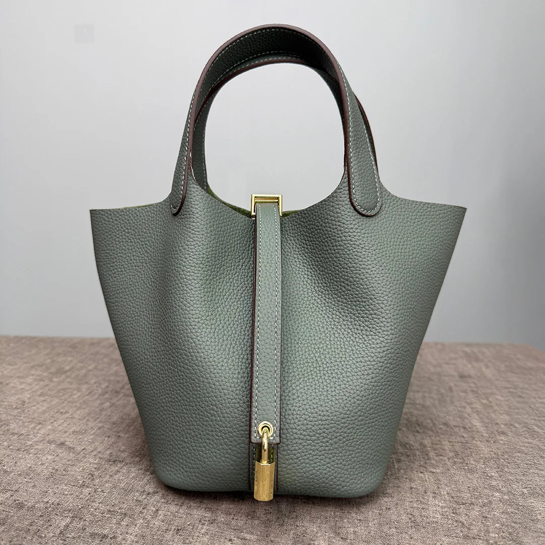 A muted sage green leather bucket bag with a dark brown strap and gold hardware.