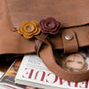 A brown leather bag features a handmade PU leather rose charm in shades of orange and purple.