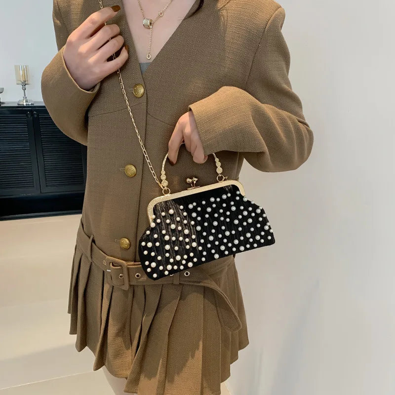 A woman wearing a camel-colored blazer and skirt holds a black studded crossbody bag with white pearls.