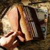 A hand holds an open genuine leather long bi-fold wallet displaying various cards and cash inside.