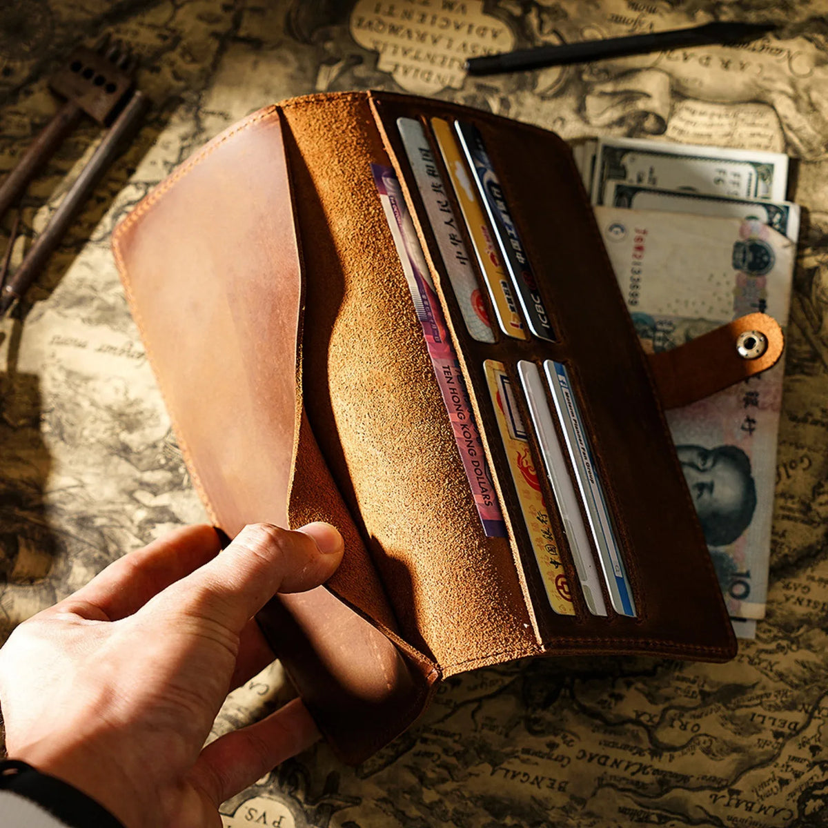 A hand holds an open genuine leather long bi-fold wallet displaying various cards and cash inside.