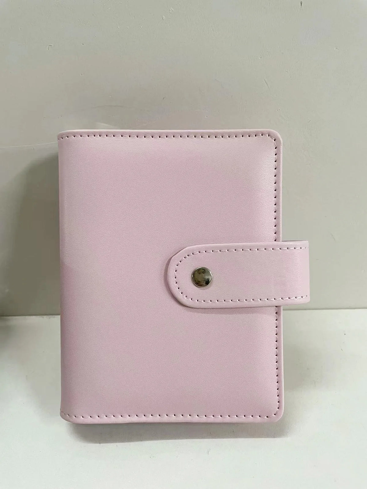 A pink leather ring binder notebook with a stitched closure.