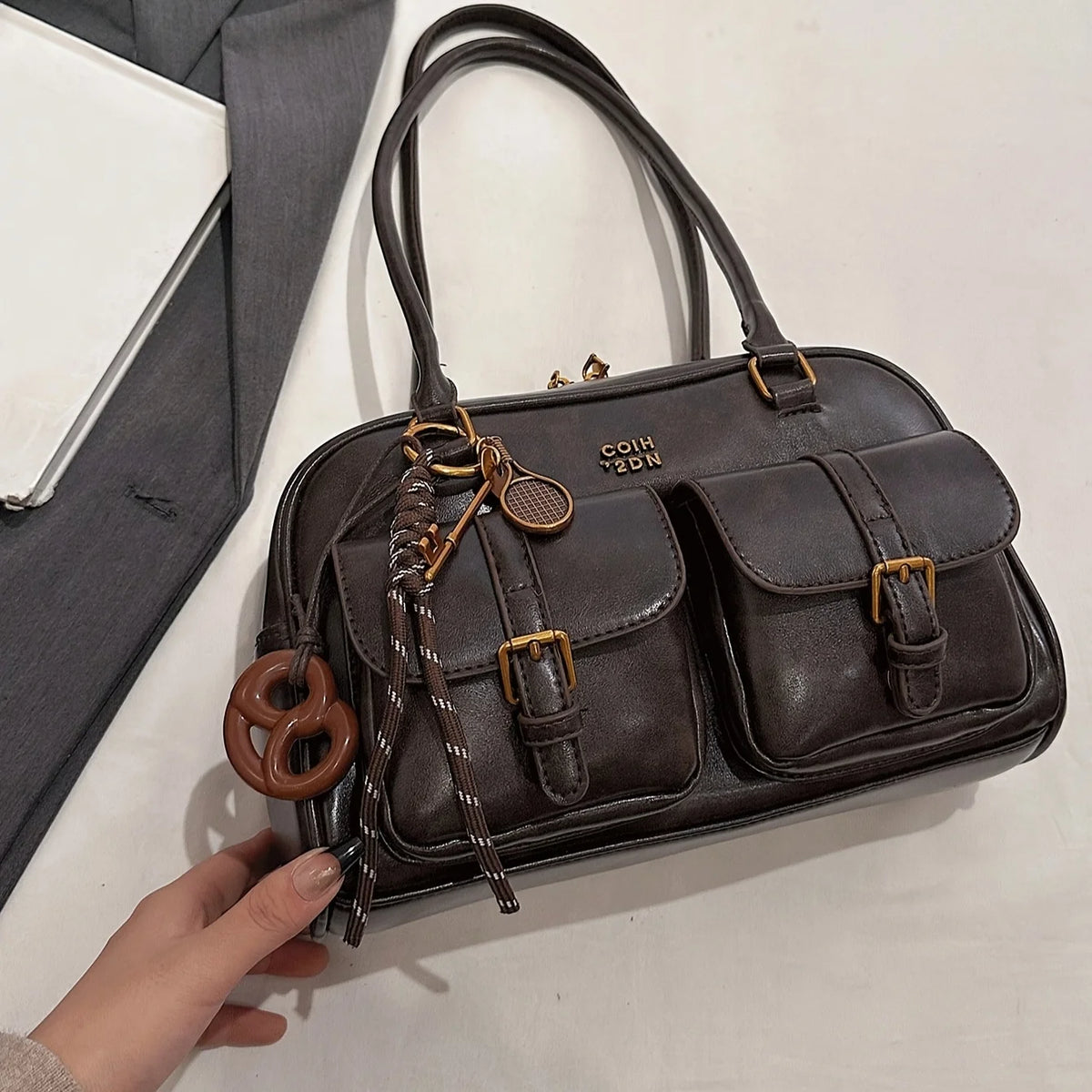 A dark brown leather vintage letter print crossbody bag with brass hardware being held by a hand.