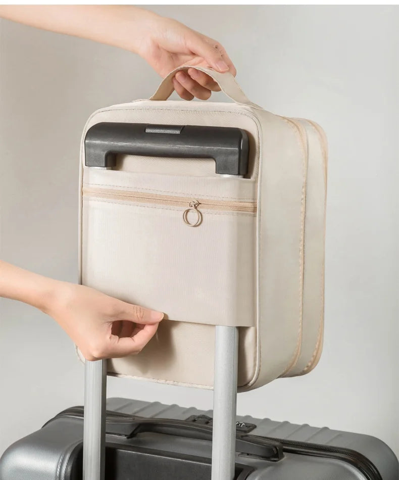 A hand is holding a beige portable luggage shoe organizer bag with a black handle and zipper.