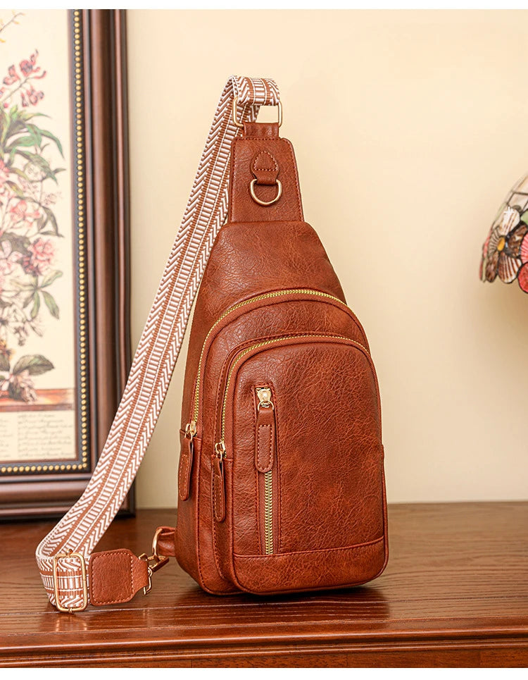 A brown PU leather crossbody sling bag with a patterned strap resting on a wooden surface.