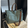 A sage green lightweight nylon tote bag with brown leather handles and strap resting on a light surface.