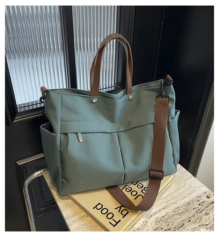 A sage green lightweight nylon tote bag with brown leather handles and strap resting on a light surface.