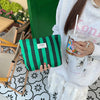 Una persona sostiene una bolsa de almacenamiento de lona a rayas verdes y negras frente a una puerta verde brillante.