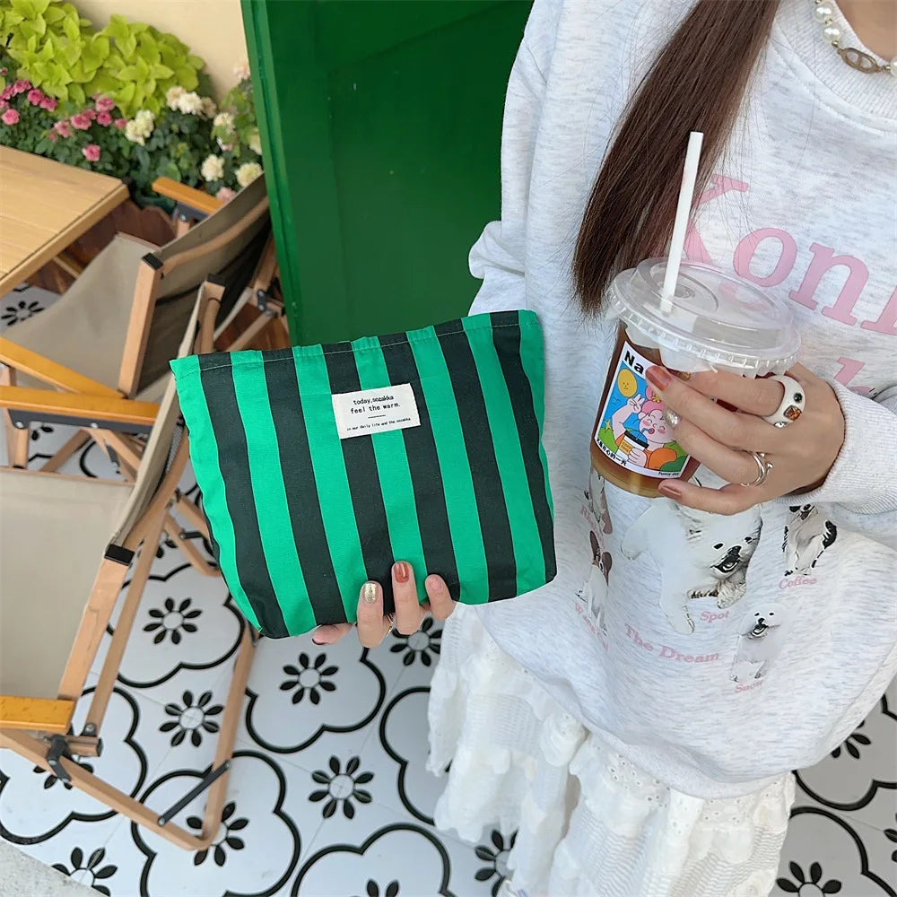 Una persona sostiene una bolsa de almacenamiento de lona a rayas verdes y negras frente a una puerta verde brillante.