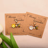 Two handmade beaded flower keychains with a yellow flower and a black bee on kraft paper cards.