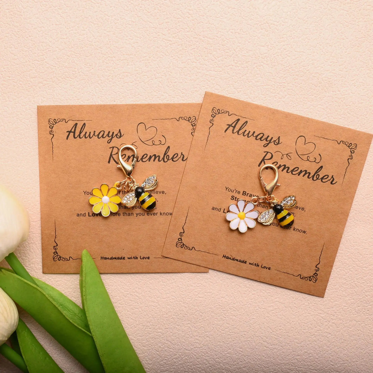 Two handmade beaded flower keychains with a yellow flower and a black bee on kraft paper cards.