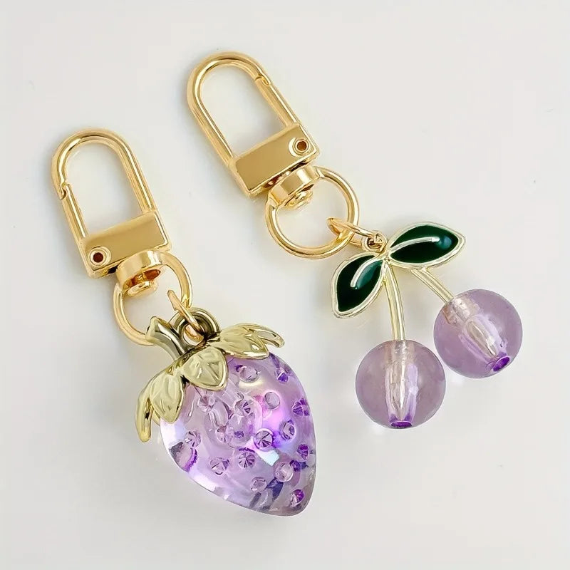 Gold-toned keychain set featuring a purple fruit charm and a green leaf charm.