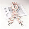 A beige and pink floral patterned nylon crossbody bag strap with a silver metal buckle displayed next to a white box.