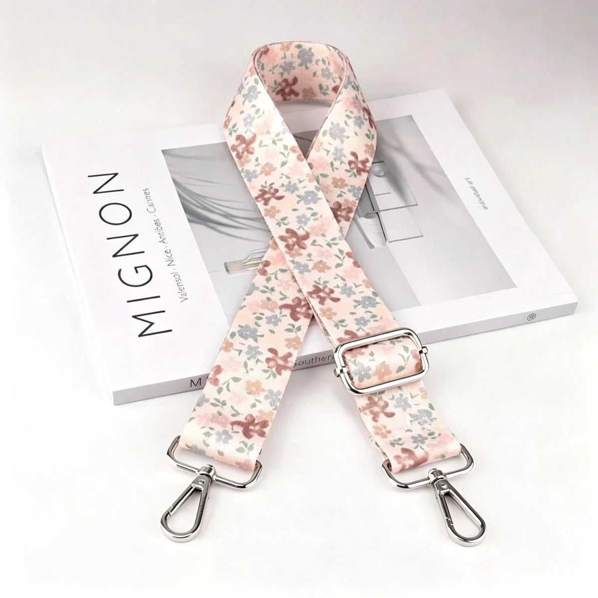A beige and pink floral patterned nylon crossbody bag strap with a silver metal buckle displayed next to a white box.