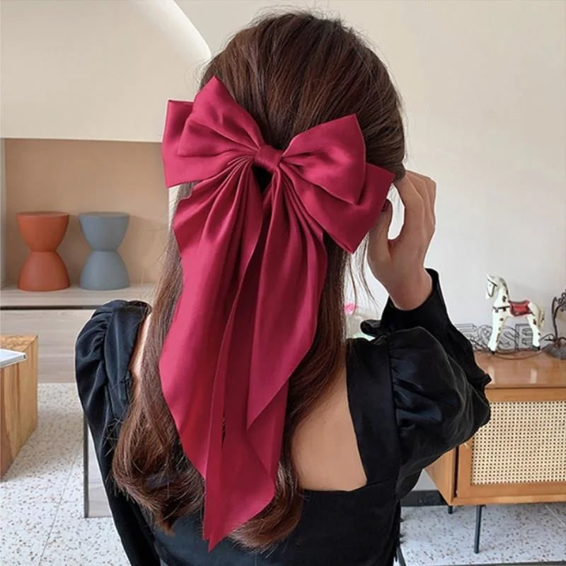 A woman with long brown hair is shown tying a deep red silk bow around her hair.