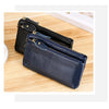 A dark navy blue genuine leather wristlet clutch wallet with a zipper closure resting on a wooden surface.