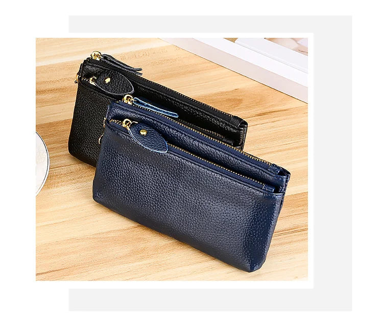 A dark navy blue genuine leather wristlet clutch wallet with a zipper closure resting on a wooden surface.