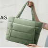 A smiling woman holds a green quilted tote bag against a light background.