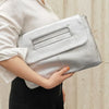 A person holds a silver sequined crossbody clutch bag against a light background.