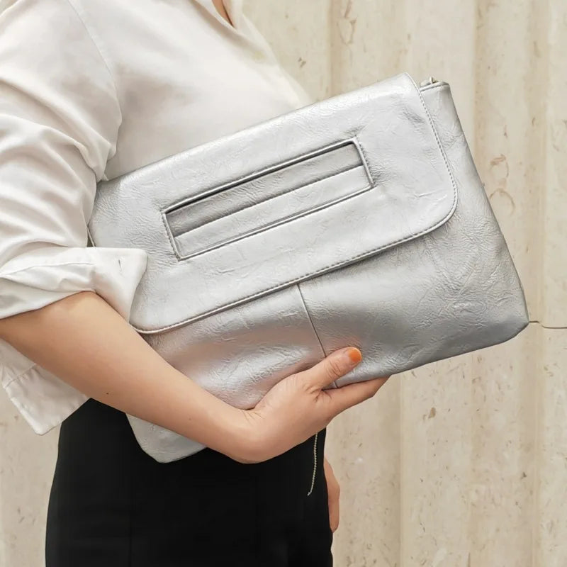 A person holds a silver sequined crossbody clutch bag against a light background.