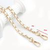 Gold-colored metal chain shoulder strap for crossbody bags shown next to a white object.